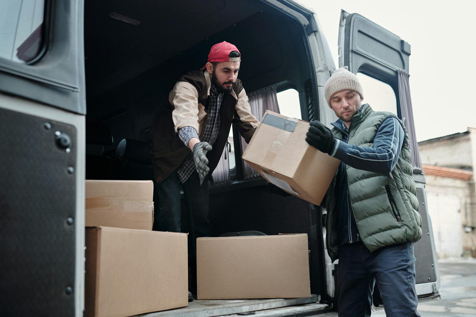 Two delivery workers unload cardboard boxes from a van, showcasing teamwork and logistics.