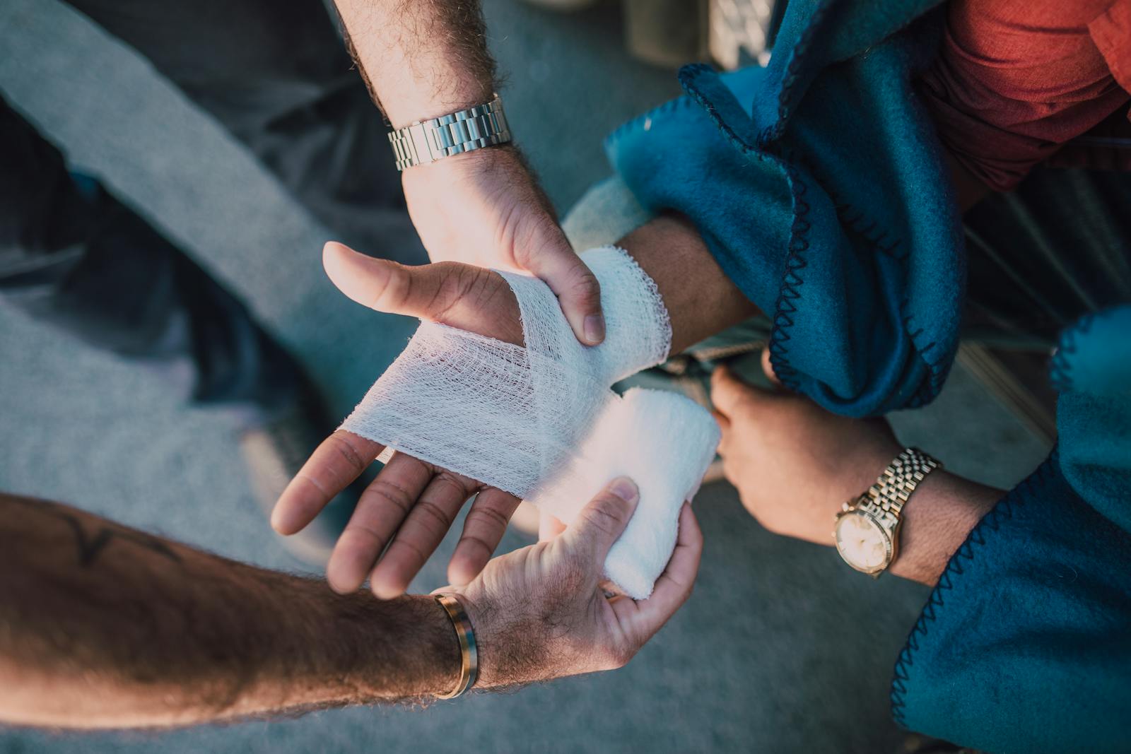 Close-up of two people bandaging an injured hand outdoors, focusing on first aid care. Personal Liability